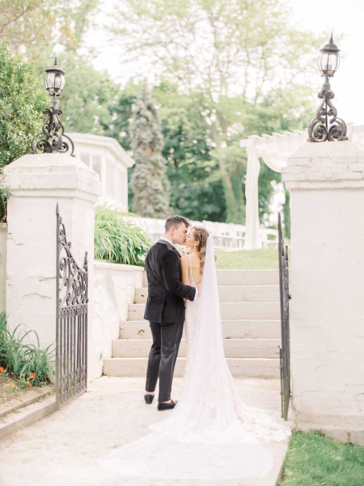 bride-and-groom-kiss-by-staircase A man and woman kissing on a staircase.